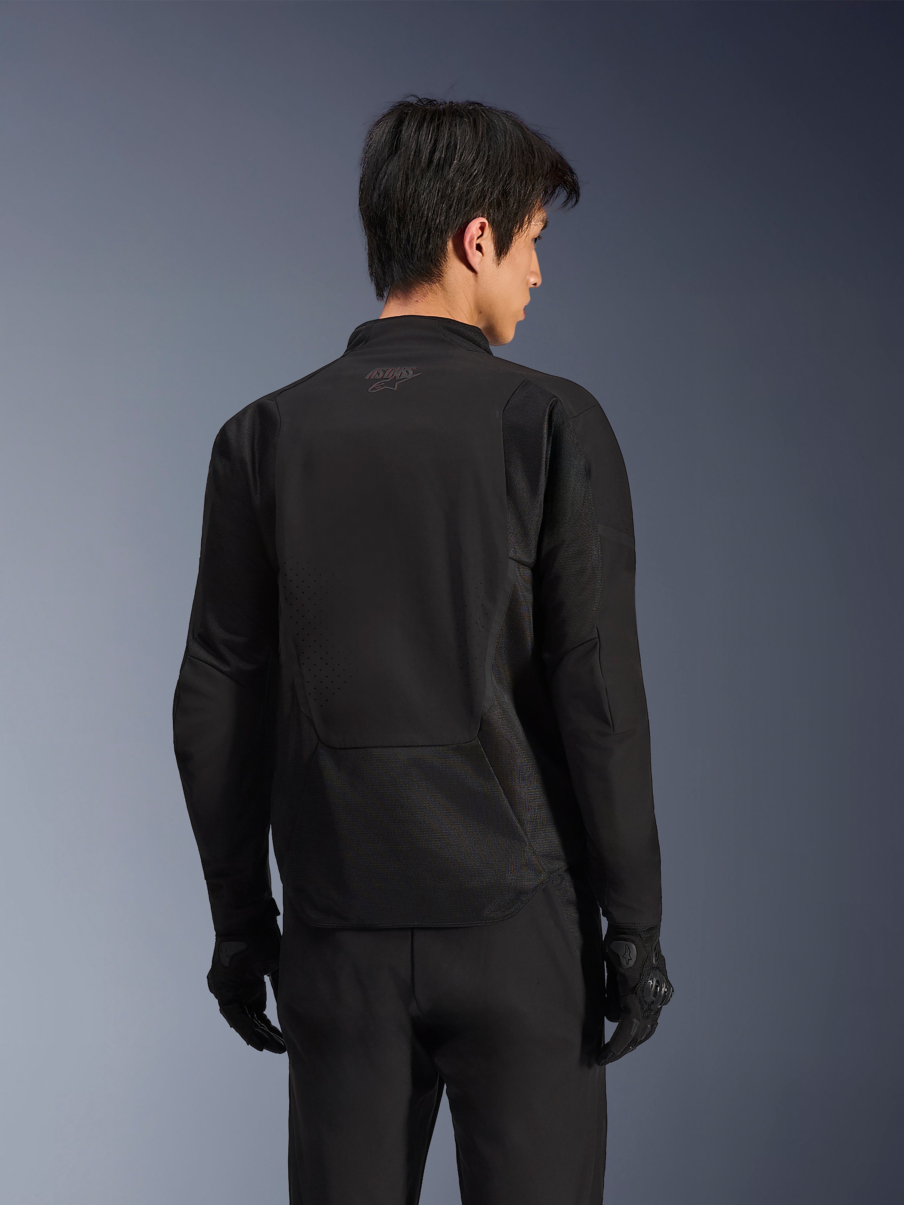 Chaqueta Alpinestars Aeroshell Airflow, Black Anthracite, vista posterior de chaqueta deportiva para motocicleta con zonas de ventilación perforadas con láser y paneles de malla 2D, parte trasera alargada para mayor cobertura, usada con guantes de conducción negros