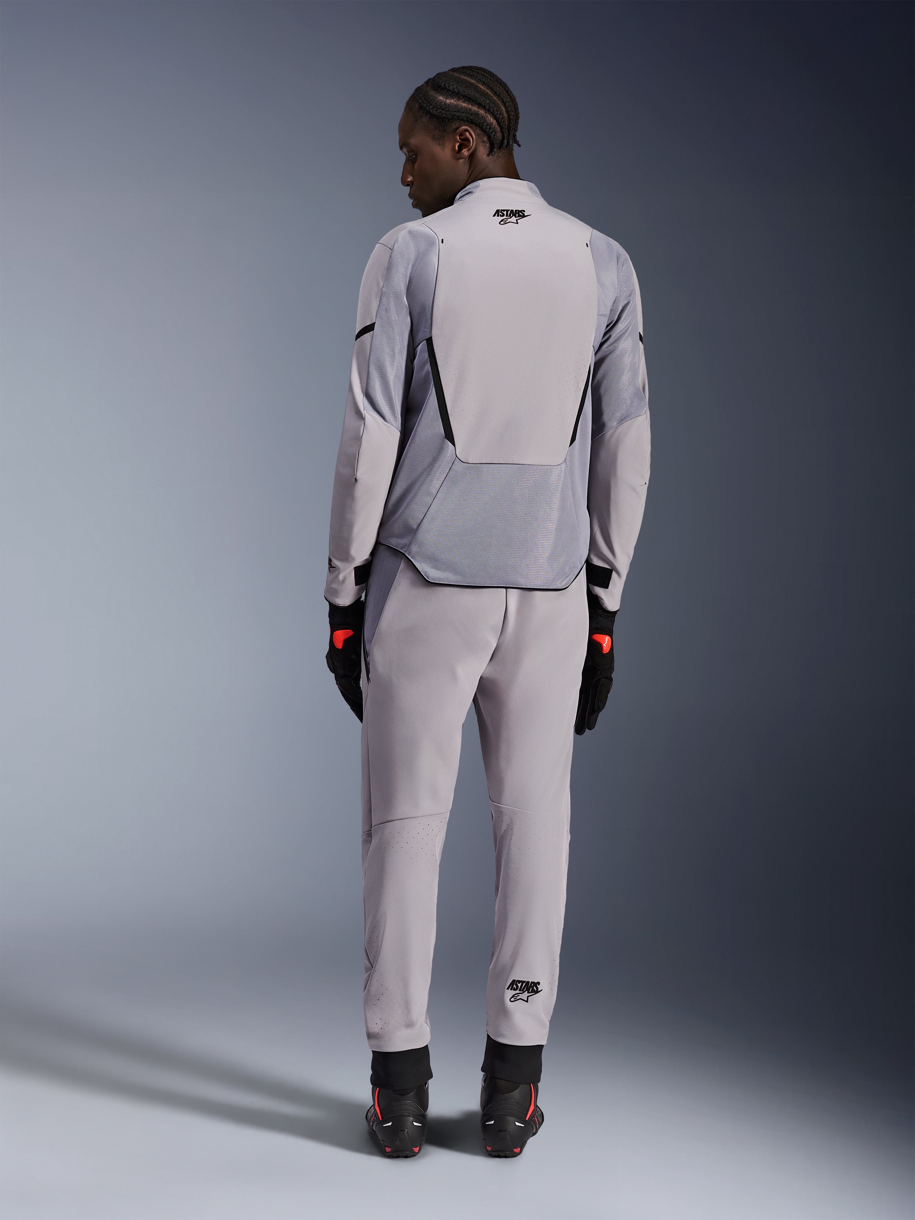 Chaqueta Alpinestars Aeroshell Airflow, Mid Gray Anthracite, vista trasera en un modelo, con paneles de malla técnica y zonas de ventilación perforadas con láser, combinada con pantalones grises a juego y equipamiento de moto negro, diseño de corte deportivo para alto rendimiento.