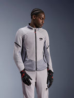 Chaqueta Alpinestars Aeroshell Airflow, Mid Gray Anthracite, usada por un modelo con pantalones textiles a juego y guantes negros con detalles rojos, con zonas perforadas por láser y paneles de malla para ventilación, diseño estilizado de ajuste deportivo para la conducción de motocicletas.