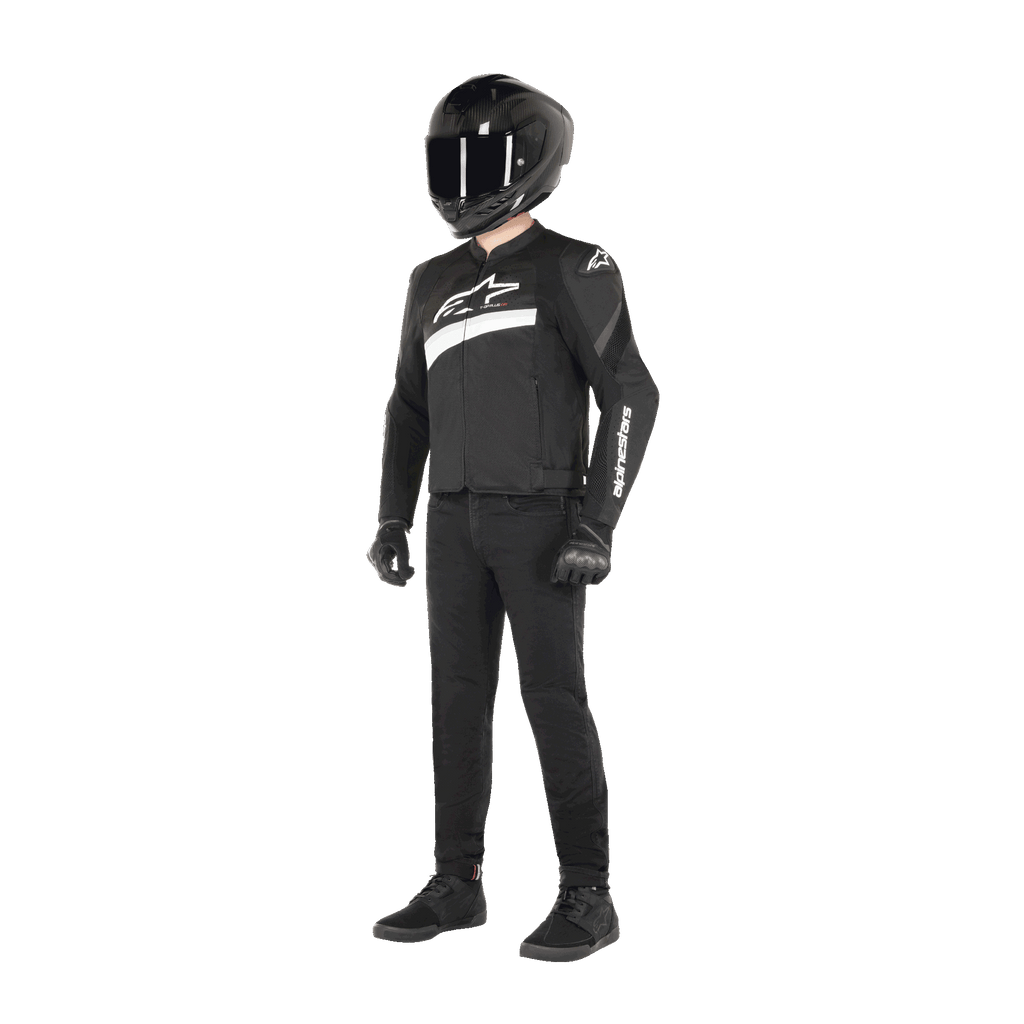 Piloto con la chaqueta Alpinestars T-GP Plus R V4 Airflow en negro y blanco, chaqueta textil de moto con paneles de malla y logotipos de Alpinestars en blanco, combinada con casco negro, guantes de moto negros, pantalones negros y calzado negro