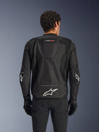 Chaqueta Alpinestars T-GP Air, negra, vista posterior de la chaqueta de moto textil, con joroba aerodinámica, paneles de ventilación de malla grandes y logotipo de Alpinestars blanco en la parte inferior de la espalda, combinada con guantes y pantalones de moto negros