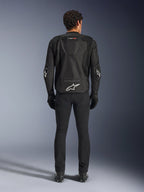 Chaqueta Alpinestars T-GP Air, negra, vista trasera de un hombre con la chaqueta textil de motociclismo, con paneles de ventilación de malla, joroba aerodinámica y logotipos blancos de Alpinestars en la parte inferior de la espalda y los codos, combinada con pantalones y guantes de conducción negros