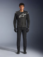 Chaqueta Alpinestars T-GP Air, chaqueta de moto textil negra con un gran logotipo Astars blanco en el pecho, usada por un modelo con pantalones de conducción y guantes negros, con paneles perforados y ventilación de malla para conducción deportiva