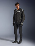 Chaqueta Alpinestars T-GP Air, chaqueta de motociclismo textil en color negro, vestida por un modelo con pantalones y guantes negros a juego, con un destacado logotipo de Alpinestars en blanco en el pecho y los hombros, paneles de malla ventilados y un ajuste deportivo derivado de las carreras