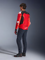 Chaqueta Alpinestars T-GP Air, vista trasera de un hombre con una chaqueta textil en rojo brillante y rojo flúor con paneles de malla negros y deslizadores blancos, combinada con vaqueros azul oscuro y calzado de moto negro, equipamiento deportivo para motociclismo.
