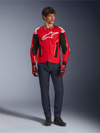 Chaqueta Alpinestars T-GP Air, rojo brillante, rojo flúor y negro, modelo masculino con equipamiento de moto completo, vaqueros azul oscuro y guantes a juego, chaqueta textil deportiva con paneles de malla perforada y logo Astars blanco, foto de estudio.