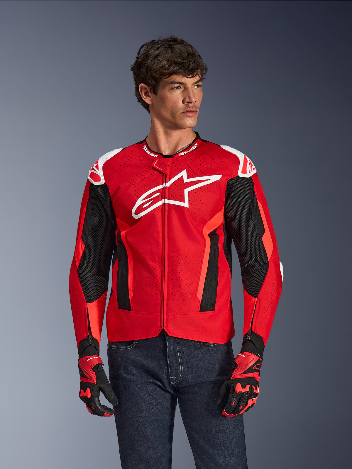 Alpinestars T-GP Air Jacket, chaqueta de motociclismo, rojo brillante y negro con logo blanco, con paneles de ventilación de malla perforada, usada con guantes a juego y vaqueros oscuros, diseño deportivo para climas cálidos