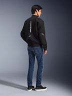 Modelo con la chaqueta Alpinestars Flight Air en color negro, vista desde atrás, combinada con vaqueros de moto azules y zapatillas negras, con marca Alpinestars vertical en blanco y paneles de ventilación de malla 3D.