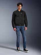 Chaqueta Alpinestars Flight Air, negra, chaqueta de moto estilo bomber de inspiración urbana con paneles de malla 3D y logotipo blanco en el pecho, usada por un modelo con vaqueros azules y zapatillas negras, indumentaria de conducción contemporánea
