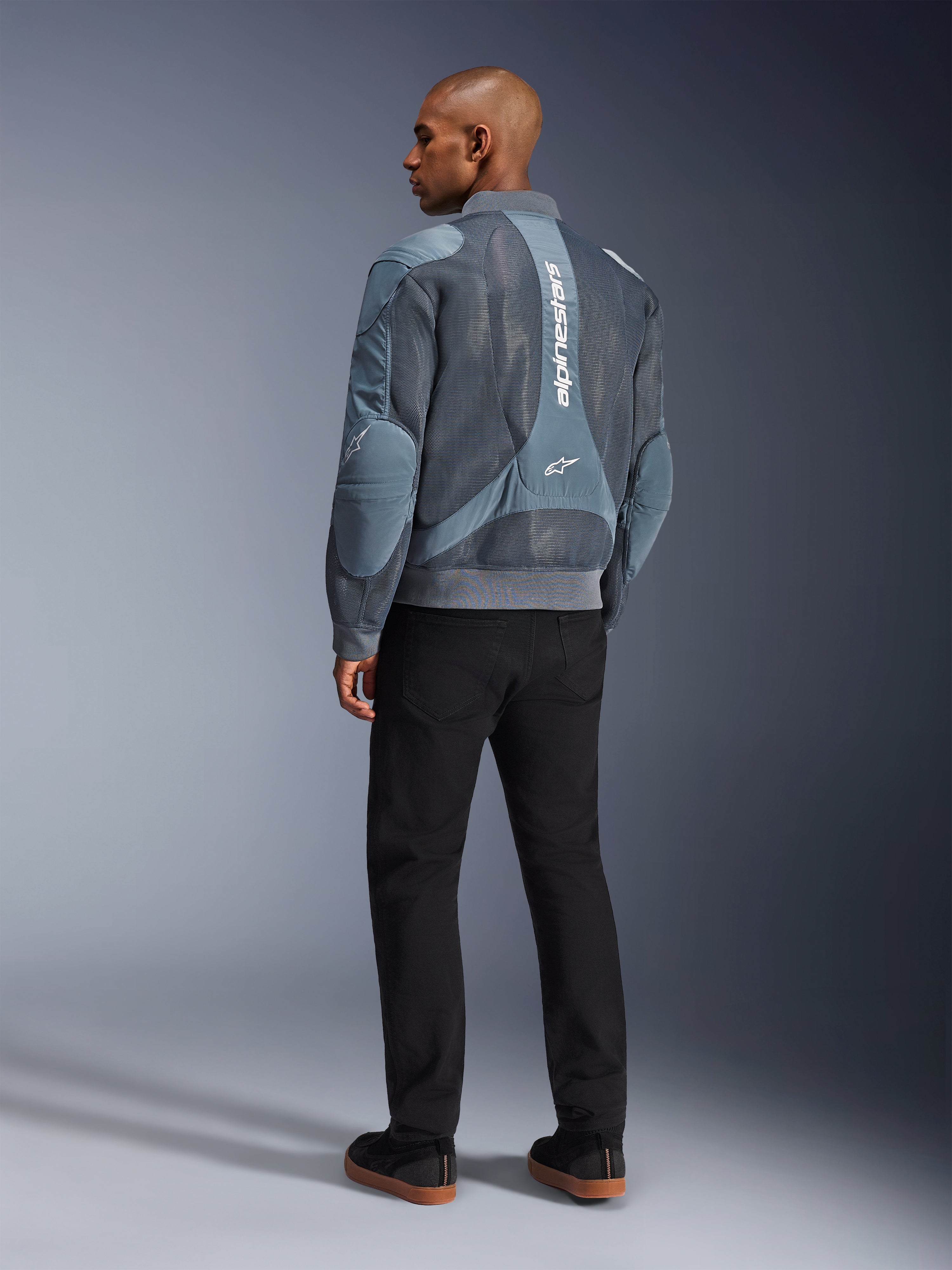 Chaqueta Alpinestars Flight Air, chaqueta de moto Storm Gray, vista posterior, con paneles de ventilación de malla 3D y marca Alpinestars vertical en blanco, combinada con pantalones negros y zapatillas negras, estilo urbano para desplazamientos diarios