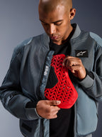 Alpinestars Flight Air Jacket en Storm Gray, chaqueta de moto urbana tipo bomber con paneles de malla 3D para ventilación, abierta para mostrar un protector de espalda Nucleon rojo, con la marca 'Alpinestars Protects' y una estética streetwear moderna