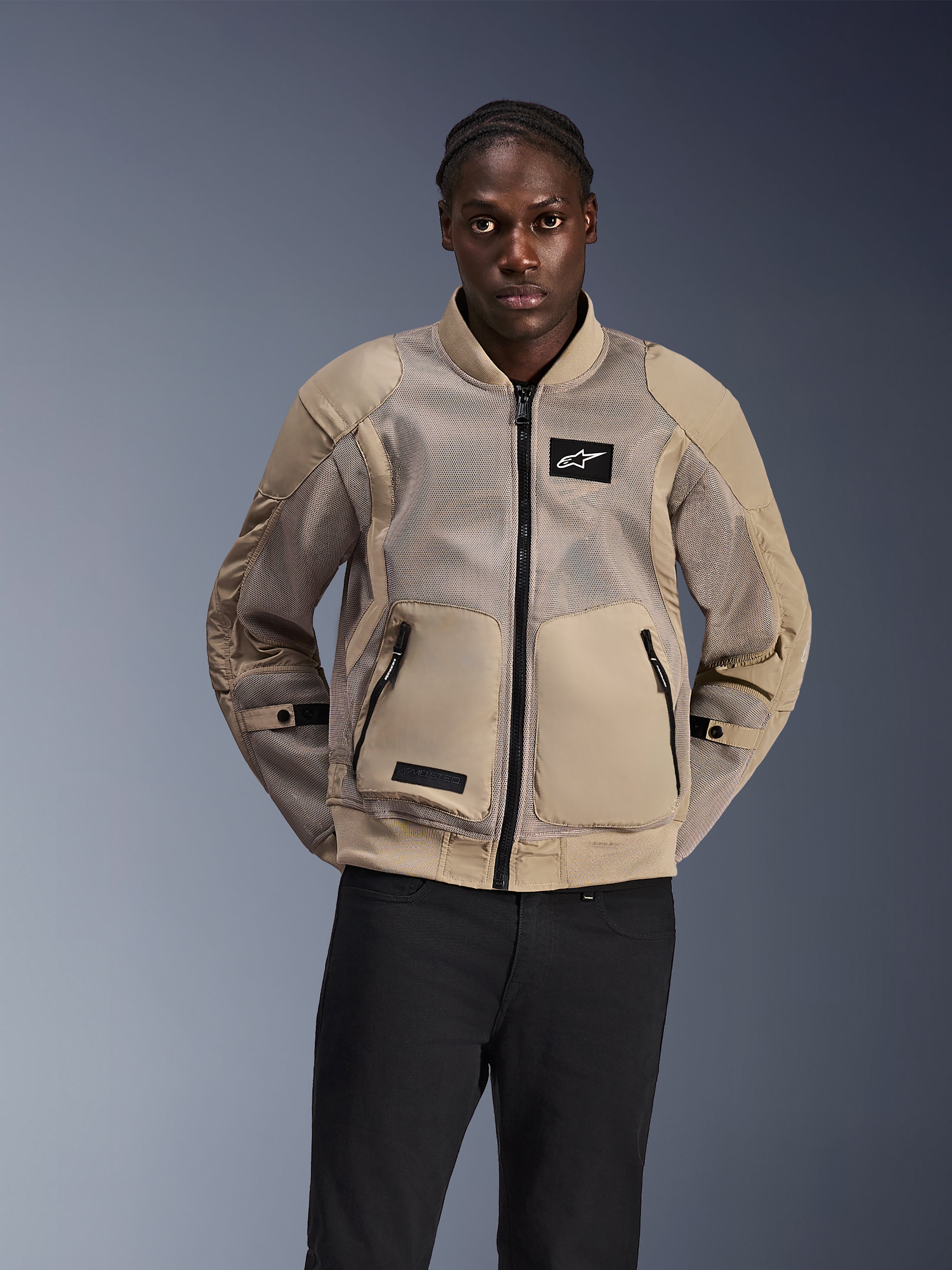 Alpinestars Flight Air Jacket, chaqueta de motociclismo urbana estilo bomber, color canela claro, con paneles de malla 3D extendidos para ventilación y bolsillos frontales grandes, usada por un hombre con pantalones negros, diseño moderno inspirado en el motociclismo para climas cálidos