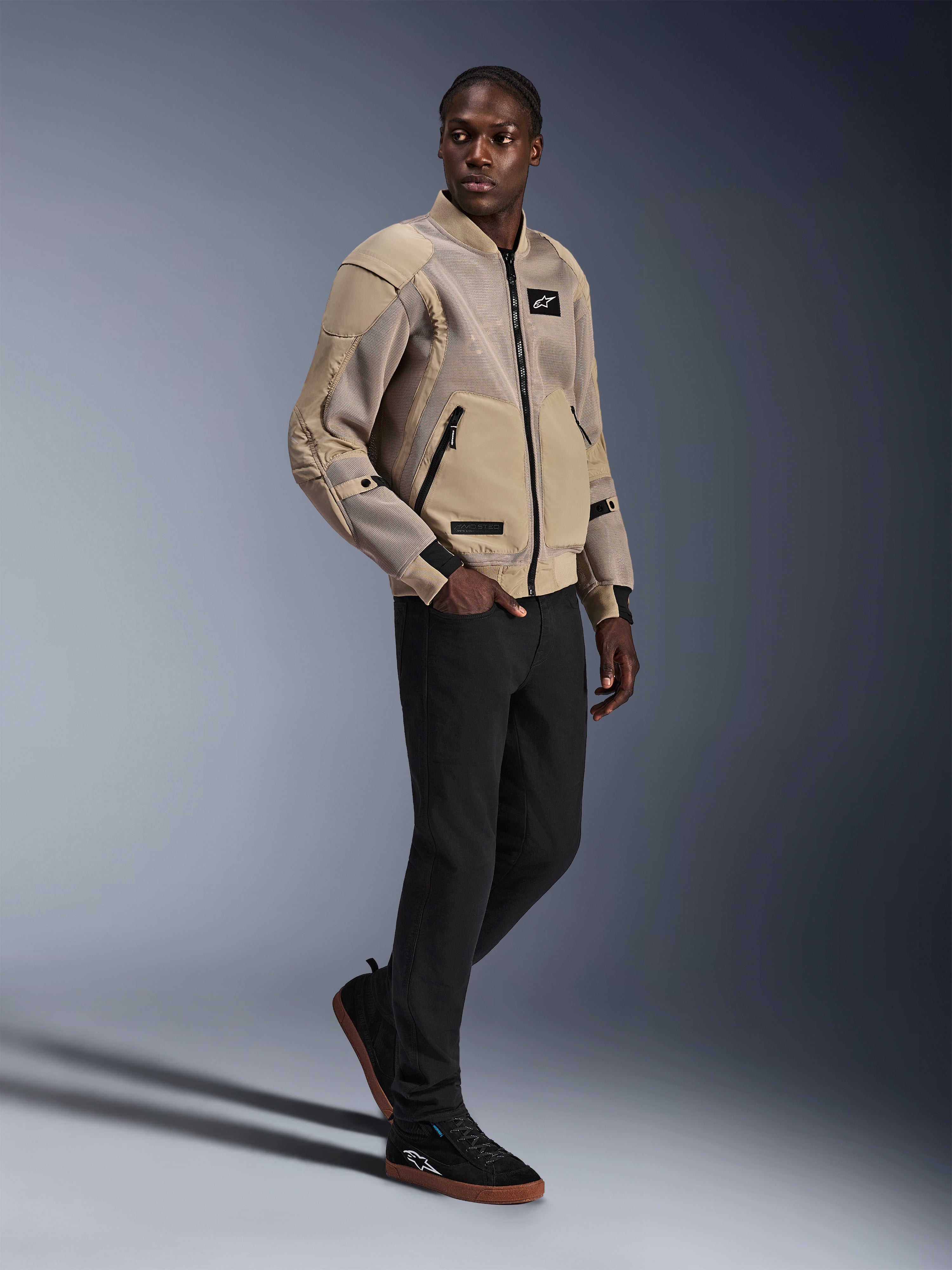 Chaqueta Alpinestars Flight Air, chaqueta urbana para motocicleta, color Aluminum, usada por un modelo con pantalones negros y zapatillas negras, con paneles de ventilación de malla 3D y un diseño estilo bomber, estilo urbano moderno para conducción en ciudad.