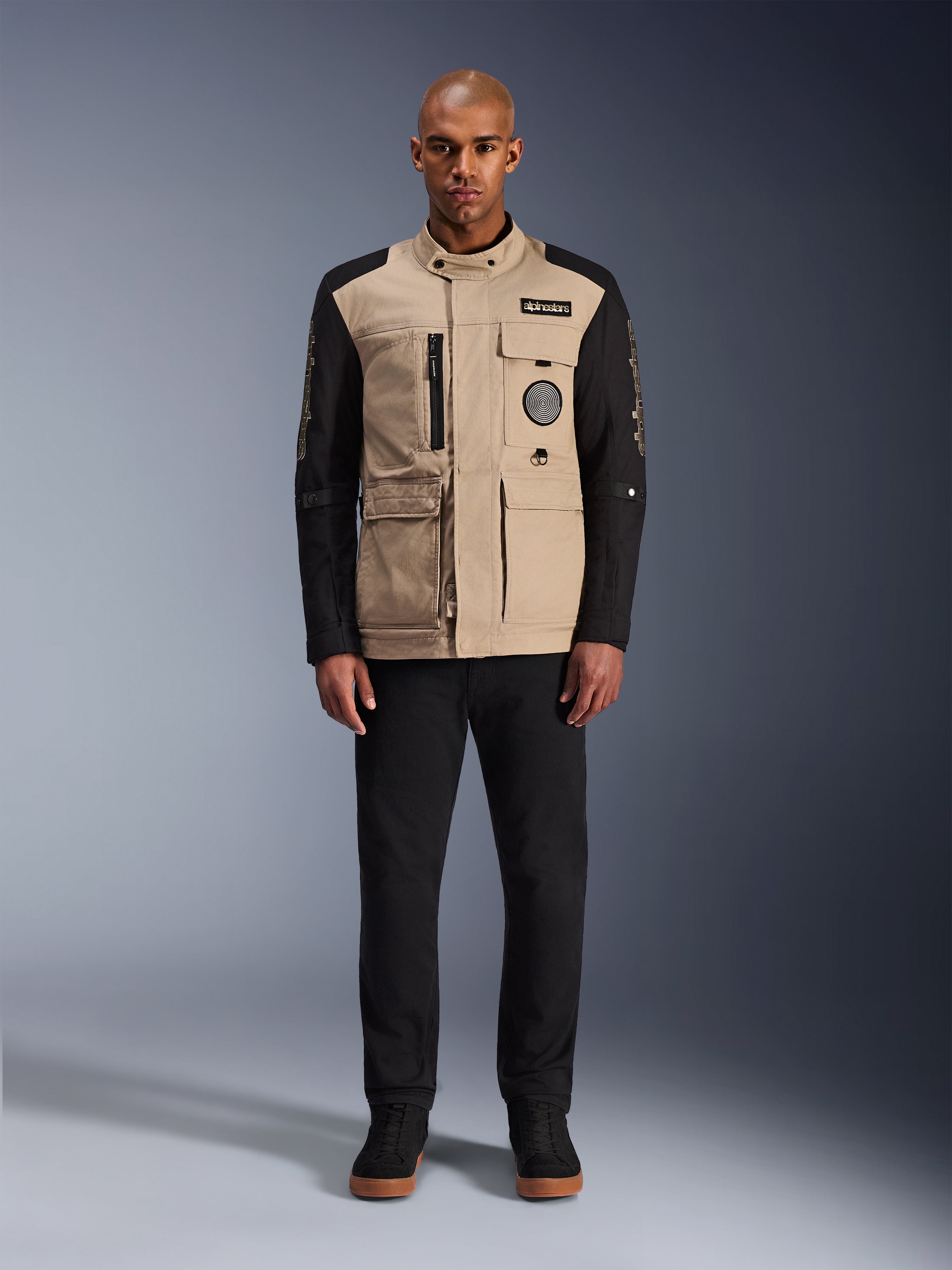 Alpinestars Dice Jacket, chaqueta de moto urbana, cuerpo color arena aluminio con mangas negras, silueta inspirada en ropa de trabajo con cuatro bolsillos frontales utilitarios, combinada con pantalones negros y zapatillas de caña alta negras, equipamiento de conducción robusto listo para la calle