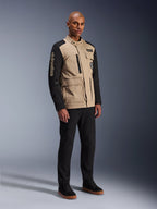 Chaqueta Alpinestars Dice, chaqueta urbana de motociclismo, Aluminum Black y tostado, diseño en dos tonos con mangas negras y torso caqui, lucida por un modelo con pantalones negros y zapatillas negras, estética de inspiración 'workwear' con bolsillos funcionales y marca bordada en la manga.
