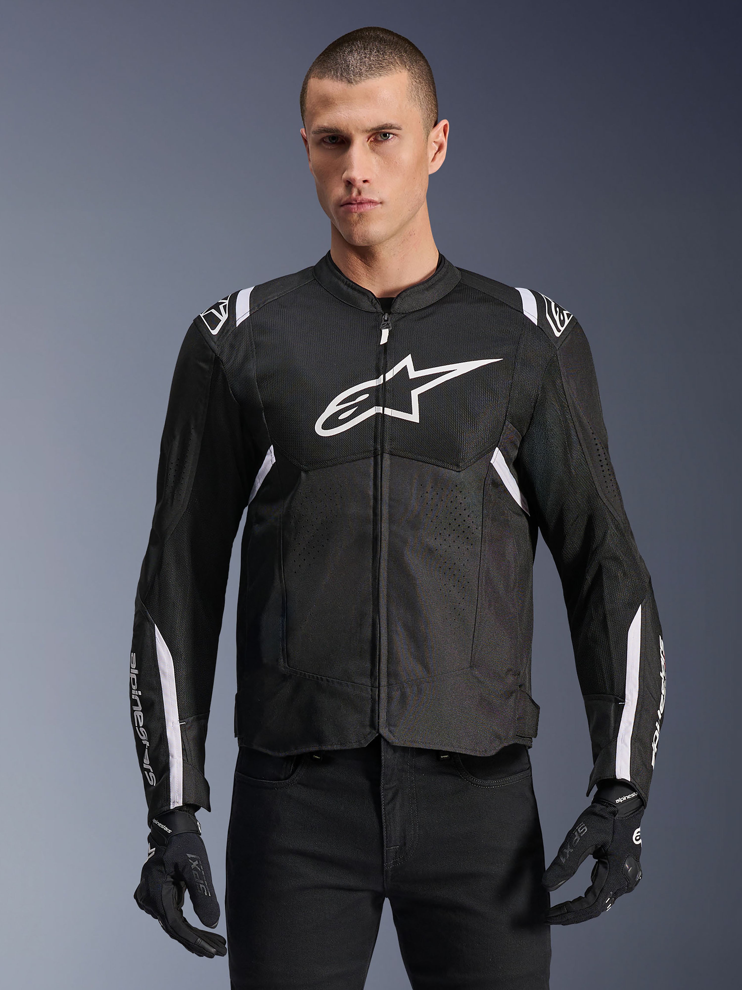 Chaqueta Alpinestars T-SPS Air V2, chaqueta de moto textil para hombre, negra con detalles en blanco, gran logo blanco en el pecho, diseño de malla perforada para ventilación, usada con pantalones y guantes negros