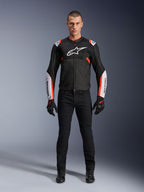 Modelo masculino con la chaqueta Alpinestars T-Sps Air V2 en negro, blanco y rojo flúor, con grandes paneles de malla técnica y logotipos blancos llamativos en el pecho y las mangas, combinada con pantalones técnicos de conducción y guantes negros, equipamiento deportivo urbano para moto