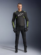 Chaqueta Alpinestars T-Sps Air V2, negro y amarillo flúor, chaqueta textil de moto con paneles de malla, usada por un modelo masculino con pantalones y guantes negros, con el logotipo blanco de Alpinestars en el pecho, equipamiento de conducción deportiva urbana