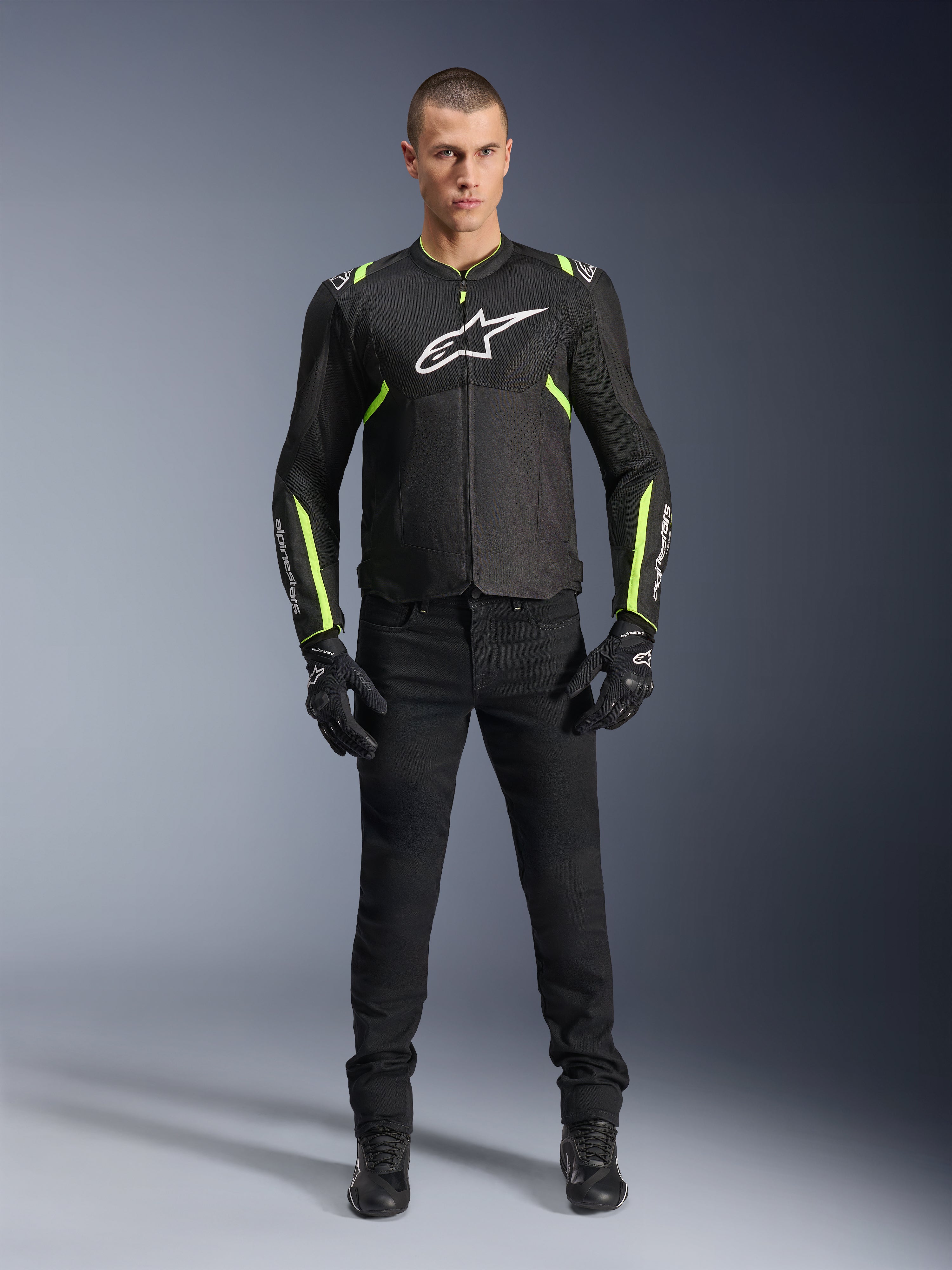 Chaqueta Alpinestars T-Sps Air V2, negro y amarillo flúor, chaqueta textil de moto con paneles de malla, usada por un modelo masculino con pantalones y guantes negros, con el logotipo blanco de Alpinestars en el pecho, equipamiento de conducción deportiva urbana