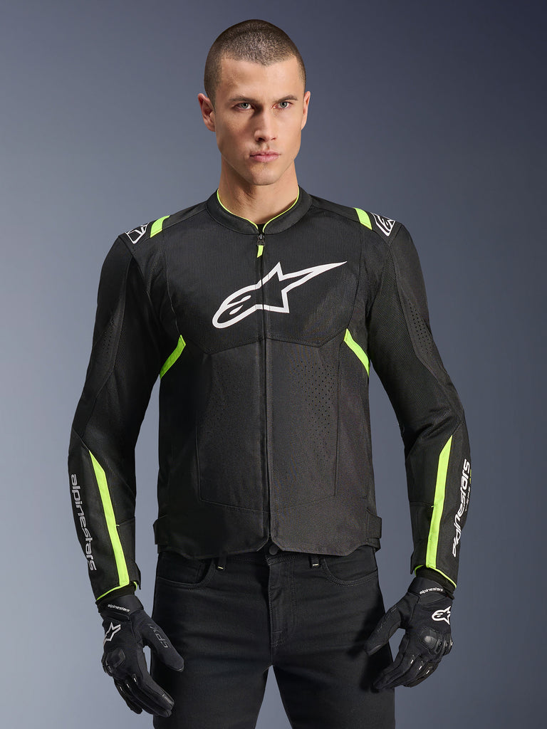 Chaqueta Alpinestars T-Sps Air V2 en Negro Amarillo Flúor, modelo masculino vistiendo la chaqueta textil ventilada con paneles de malla y logotipo blanco en el pecho, combinada con guantes de motorista negros, equipamiento urbano para motocicleta