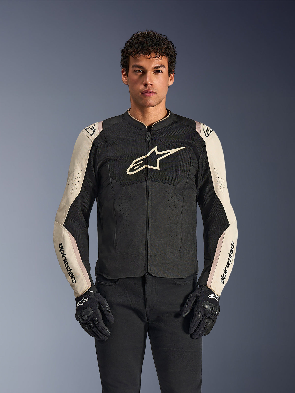 Alpinestars T-SPS Air V2 Jacket, chaqueta de moto, negro y mastic aluminum, modelo masculino vistiendo la chaqueta con pantalones y guantes negros, con paneles de malla para ventilación, logotipo grande de Alpinestars en el pecho y diseño deportivo ajustado