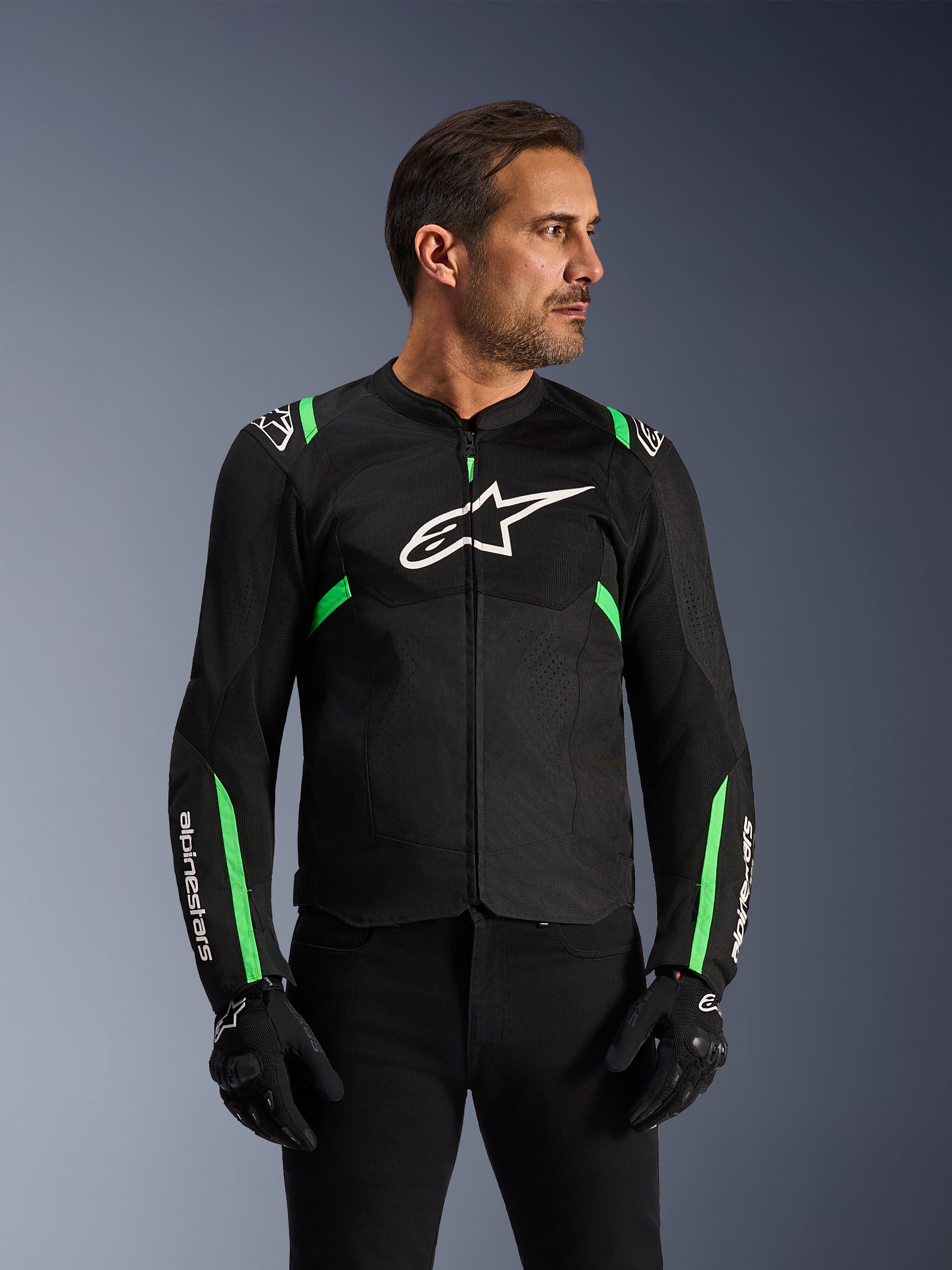 Chaqueta Alpinestars T-SPS Air V2, chaqueta de moto, negro y verde flúor, usada por un modelo con guantes y pantalones de conducción negros, con el logo blanco de Alpinestars en el pecho y detalles en verde neón en hombros y mangas, paneles de malla técnica para ventilación, diseño de corte deportivo para conducción urbana