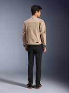 Vista posterior de un modelo con la chaqueta Alpinestars Bruiser en color marrón, una chaqueta de moto urbana con un diseño inspirado en la ropa de trabajo, con detalles de ojales metálicos en la espalda y ajustadores en la cintura, combinada con pantalones negros y zapatillas, estilo de conducción urbana contemporáneo.