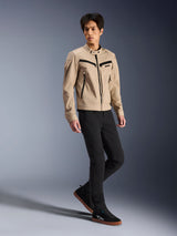 Chaqueta Alpinestars Bruiser, chaqueta urbana de motociclismo, color canela, lucida por un modelo masculino con pantalones negros ajustados y zapatillas negras, construcción textil inspirada en ropa de trabajo con detalles de cremalleras negras, estilo urbano contemporáneo.