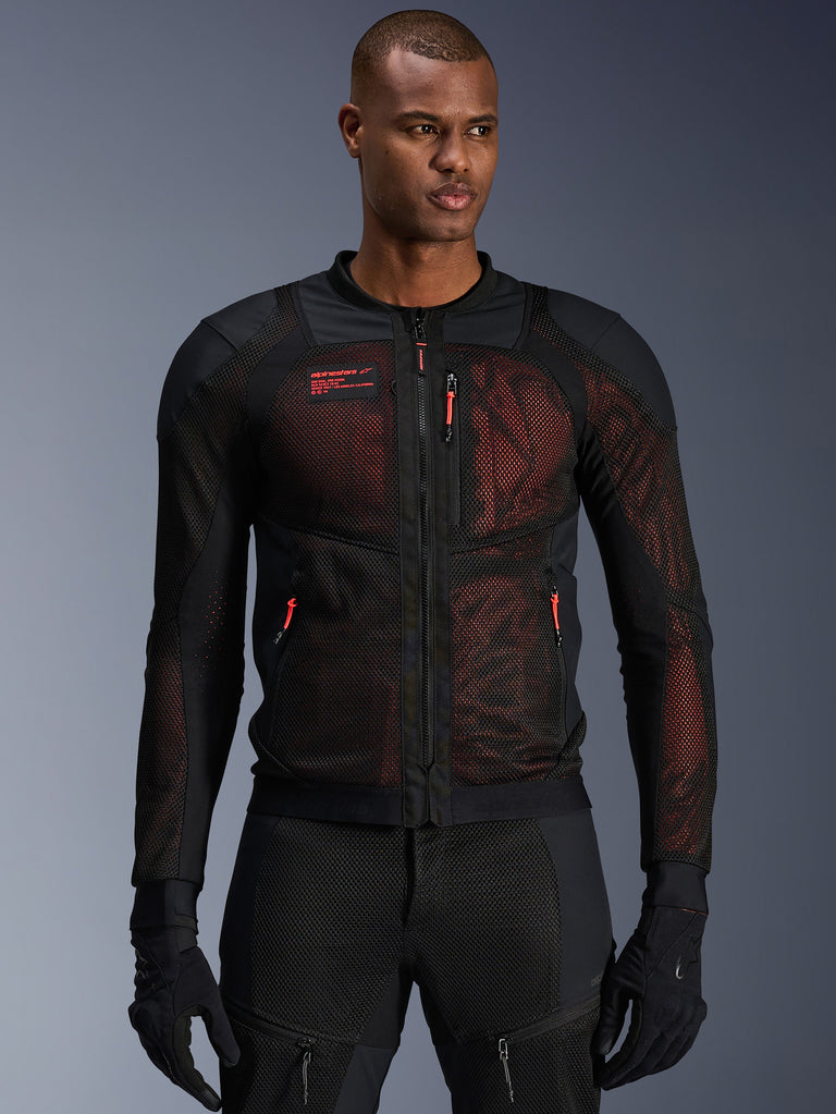 Chaqueta Alpinestars Troop-Air Pro, chaqueta técnica de malla blindada para moto en negro y rojo flúor, usada por un modelo, con grandes paneles de ventilación de malla, capa inferior roja y tiradores de cremallera rojos, estilo de conducción urbana.