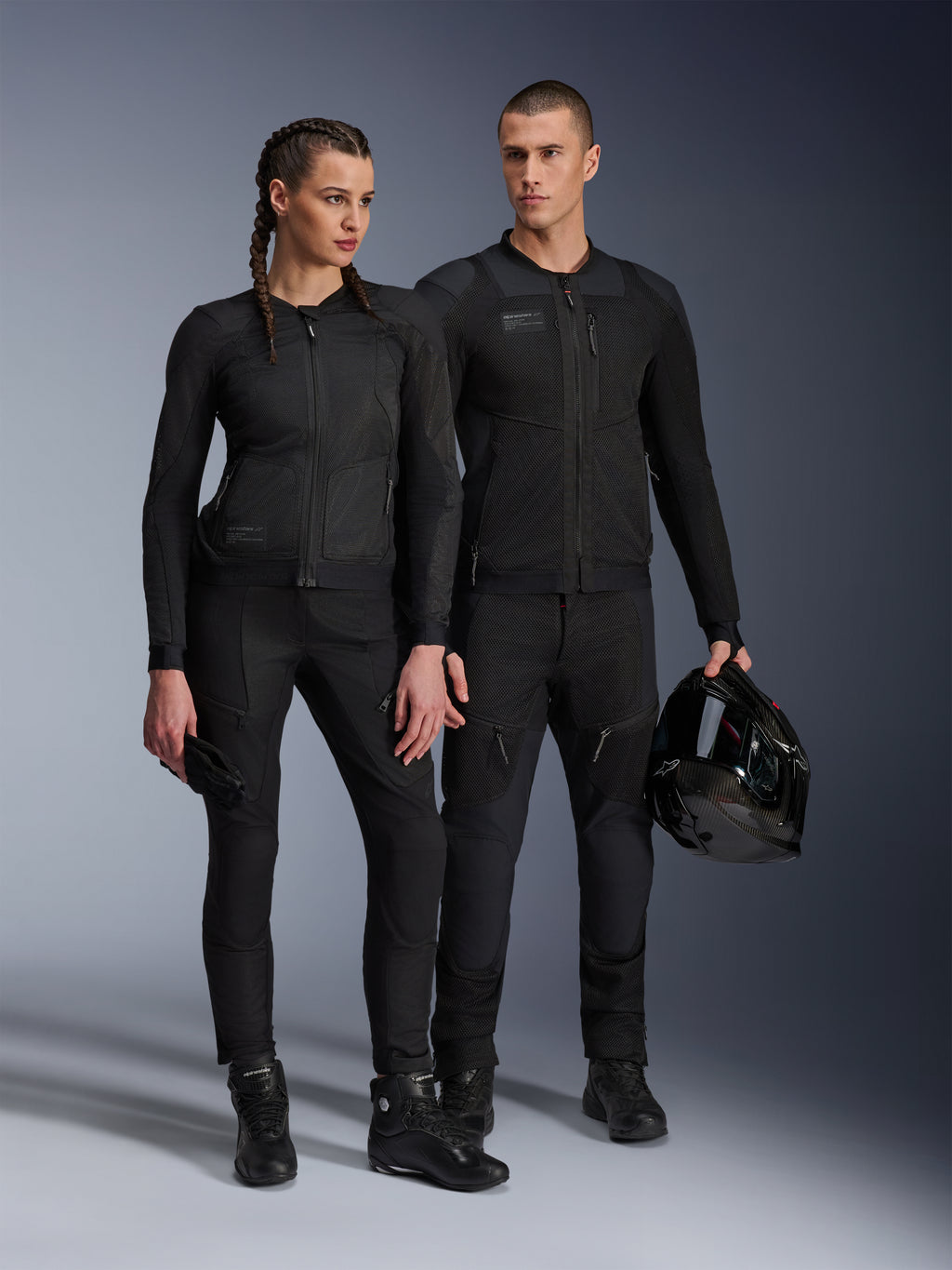 Chaqueta Alpinestars Stella Troop-Air, hombre y mujer con equipamiento técnico de motociclismo a juego en color negro, con construcción de malla para el flujo de aire, pantalones y botas negras, hombre sosteniendo un casco negro, ropa de conducción urbana