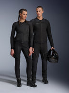 Chaqueta Alpinestars Stella Troop-Air, hombre y mujer con equipamiento técnico de motociclismo a juego en color negro, con construcción de malla para el flujo de aire, pantalones y botas negras, hombre sosteniendo un casco negro, ropa de conducción urbana