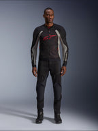 Modelo masculino con la chaqueta Alpinestars Troop-Air en color Negro Gris Ceniza y Rojo Brillante, chaqueta de malla técnica para moto con un prominente logotipo rojo en el pecho, combinada con pantalones y botas de moto negros, ropa de conducción urbana