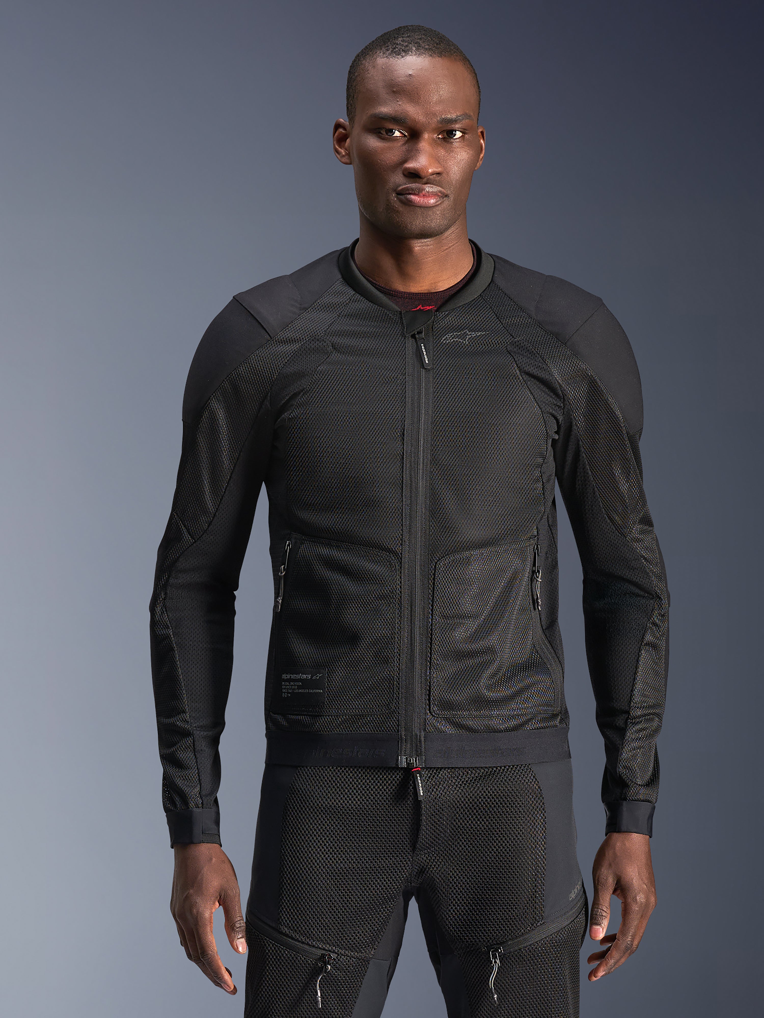 Chaqueta Alpinestars Troop-Air, chaqueta de malla negra para moto, usada por un modelo con pantalones de malla negros a juego, construcción de malla técnica 2D transpirable con paneles reforzados en los hombros, cremallera frontal, equipamiento moderno de conducción urbana