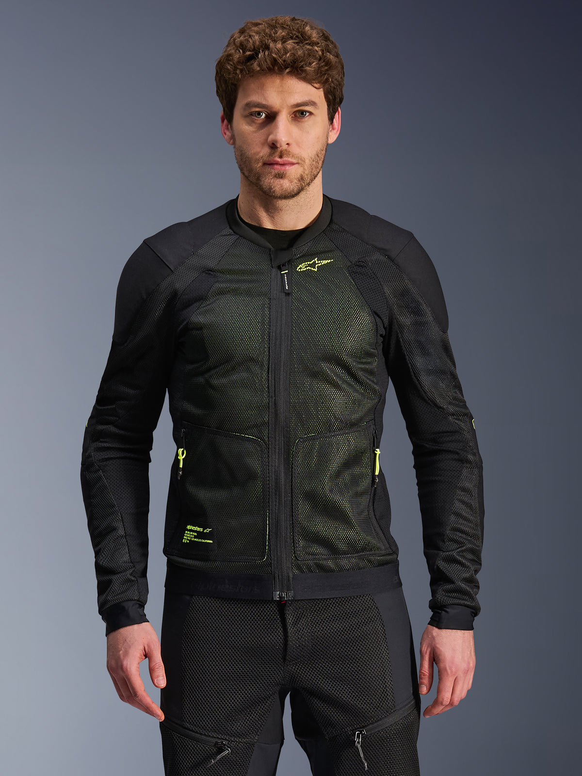 Chaqueta Alpinestars Troop-Air, negro y amarillo flúor, lucida por un modelo masculino, con construcción de malla ligera, cremalleras y marca en amarillo neón, chaqueta técnica ventilada de moto para conducción urbana
