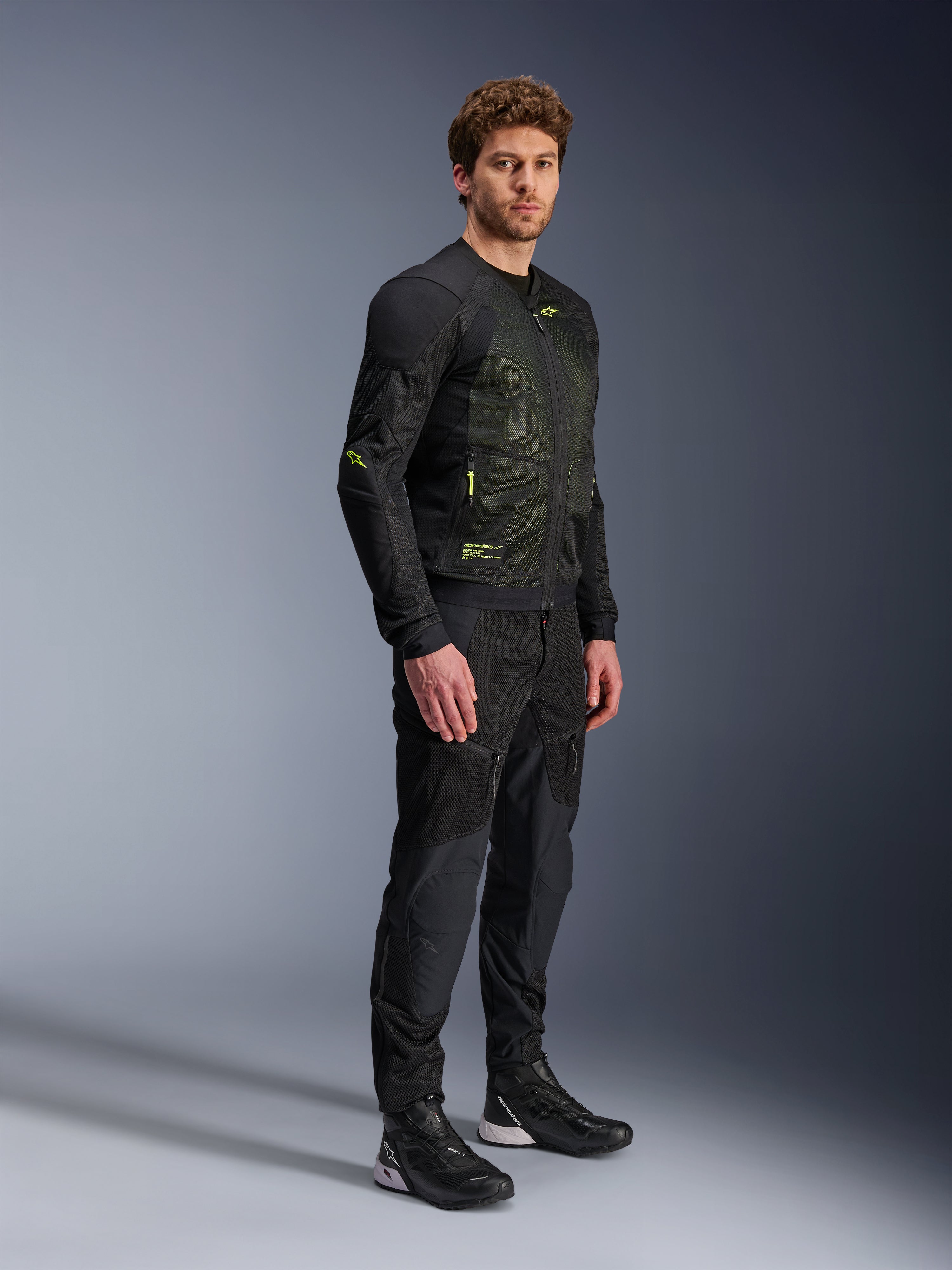 Chaqueta Alpinestars Troop-Air, chaqueta de malla para moto, negro y amarillo flúor, usada por un modelo con pantalones negros y calzado de conducción a juego, cuenta con una construcción de malla de alto flujo de aire con detalles amarillos fluorescentes en el pecho y las mangas, diseño técnico ligero para conducción en carretera