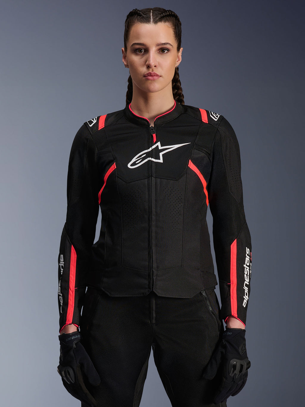 Chaqueta para mujer Alpinestars Stella T-Sps Air V2, negro y rosa diva, chaqueta textil para moto con paneles de malla transpirable y detalles en rosa, logo blanco de Alpinestars en el pecho, usada por una modelo con pantalones y guantes de motociclismo negros