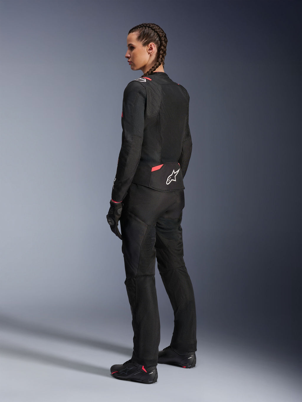 Chaqueta textil de moto Alpinestars Stella T-Sps Air v2 para mujer, negro y rosa diva, vista lateral trasera, con amplios paneles de malla para ventilación y el logo de estrella blanca en la espalda, combinada con pantalones de motociclismo, guantes y botas negras a juego.