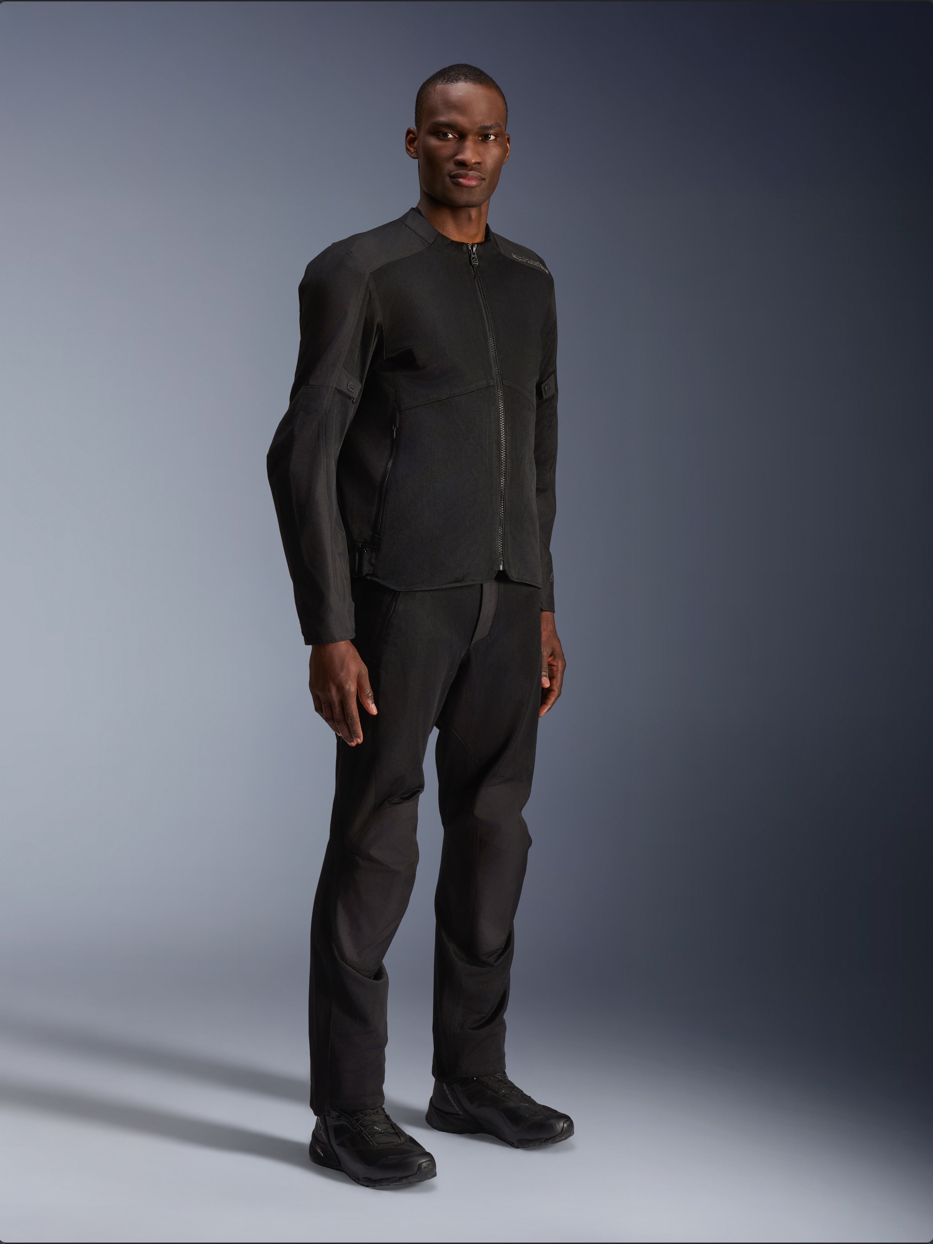 Chaqueta Alpinestars C-1 Air, negra, lucida por un modelo con pantalones de moto y calzado negros a juego, con amplios paneles de malla técnica para el flujo de aire, estética urbana limpia y ajuste estilizado.