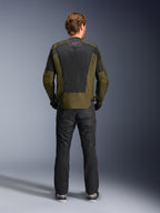 Vista posterior de un motociclista con la chaqueta Alpinestars C-1 Air en color caqui y negro, con un gran panel de malla técnica en la espalda para ventilación, combinada con pantalones de moto negros, equipamiento de conducción urbana contemporánea.
