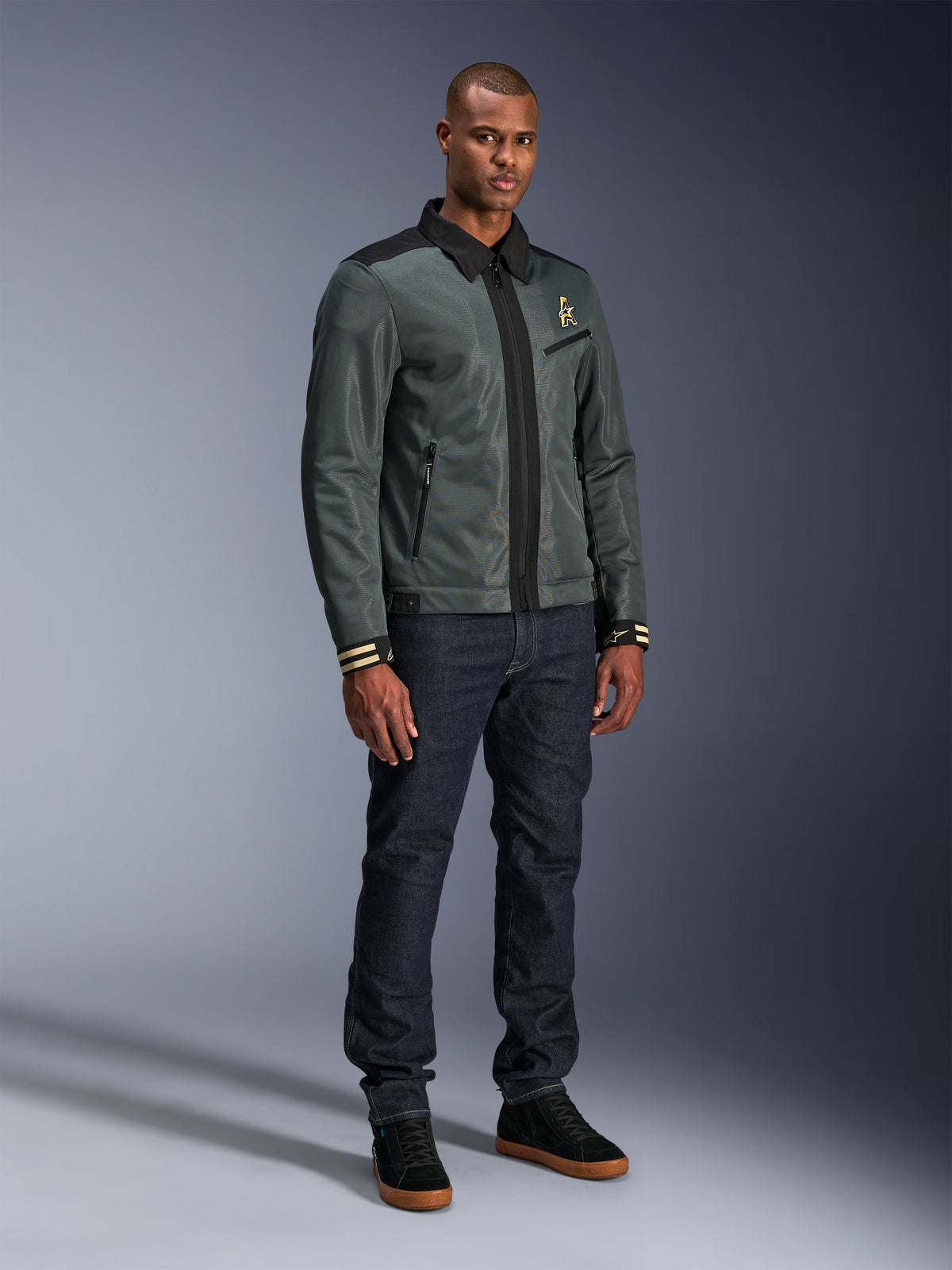 Chaqueta Alpinestars Ignite Air, Urban Gray Black Blue, chaqueta de moto urbana, vestida por un modelo con vaqueros oscuros y zapatillas negras, con cuerpo de malla, cuello de camisa tradicional, silueta inspirada en Harrington y detalles de la marca Alpinestars en dorado.
