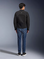 Vista trasera de un modelo con la chaqueta Alpinestars Provoke, chaqueta de moto textil técnica negra, combinada con vaqueros de moto azules y zapatillas negras, mostrando la confección de la espalda y el pequeño logotipo blanco de Alpinestars, diseño urbano contemporáneo