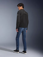 Chaqueta Alpinestars Provoke, chaqueta de moto urbana negra, vista de tres cuartos desde atrás usada por un modelo, combinada con pantalones vaqueros azules y zapatillas negras, con inserciones de softshell ripstop y logotipos blancos de Alpinestars en la manga y la espalda.