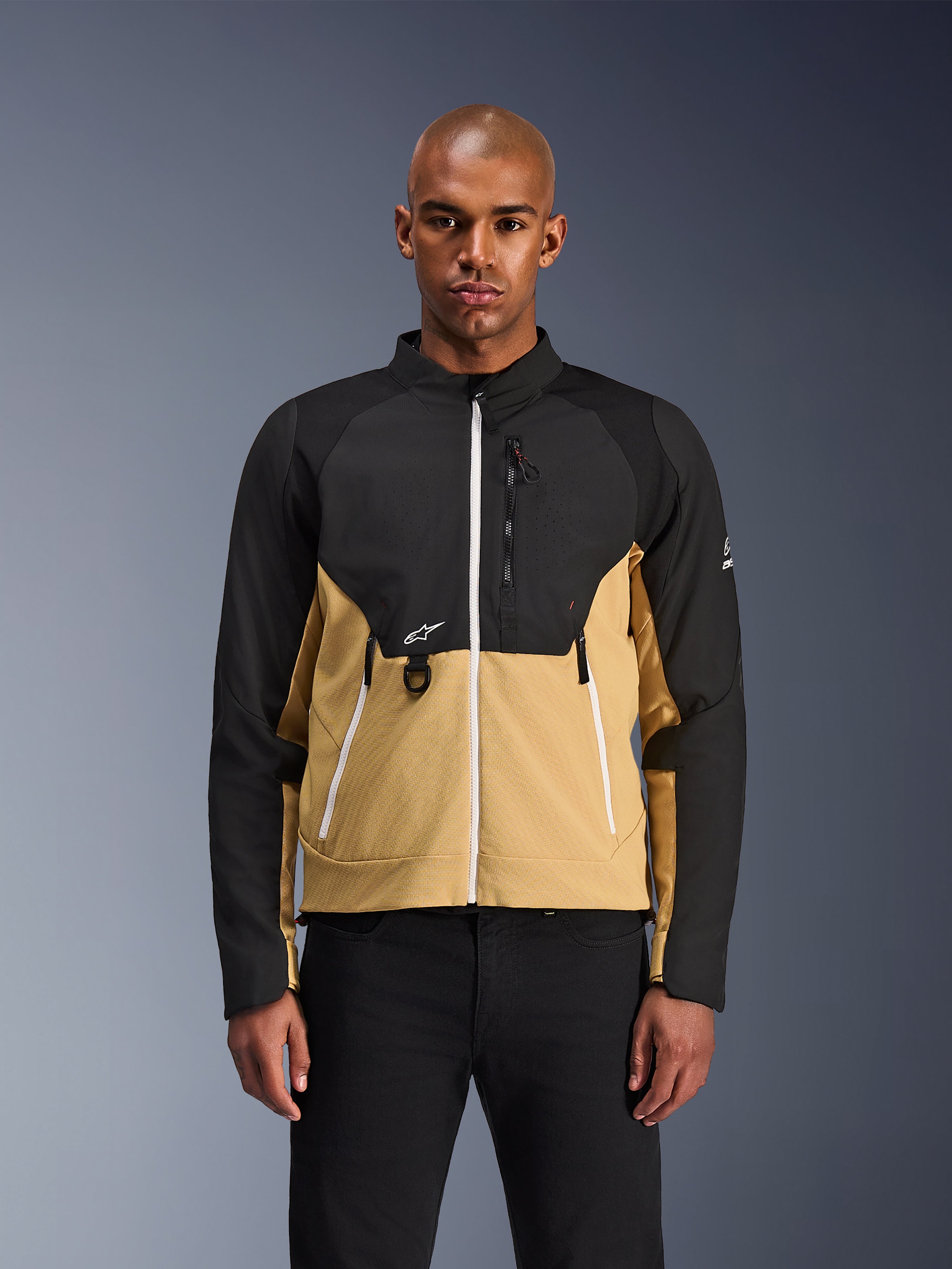 Chaqueta Alpinestars Provoke, chaqueta de moto urbana, negro y camel, vista frontal en un modelo masculino, con un diseño de dos tonos, cremalleras blancas, bolsillo con cremallera en el pecho con anilla en D y pequeño logotipo blanco de Alpinestars, ropa urbana contemporánea para motoristas.