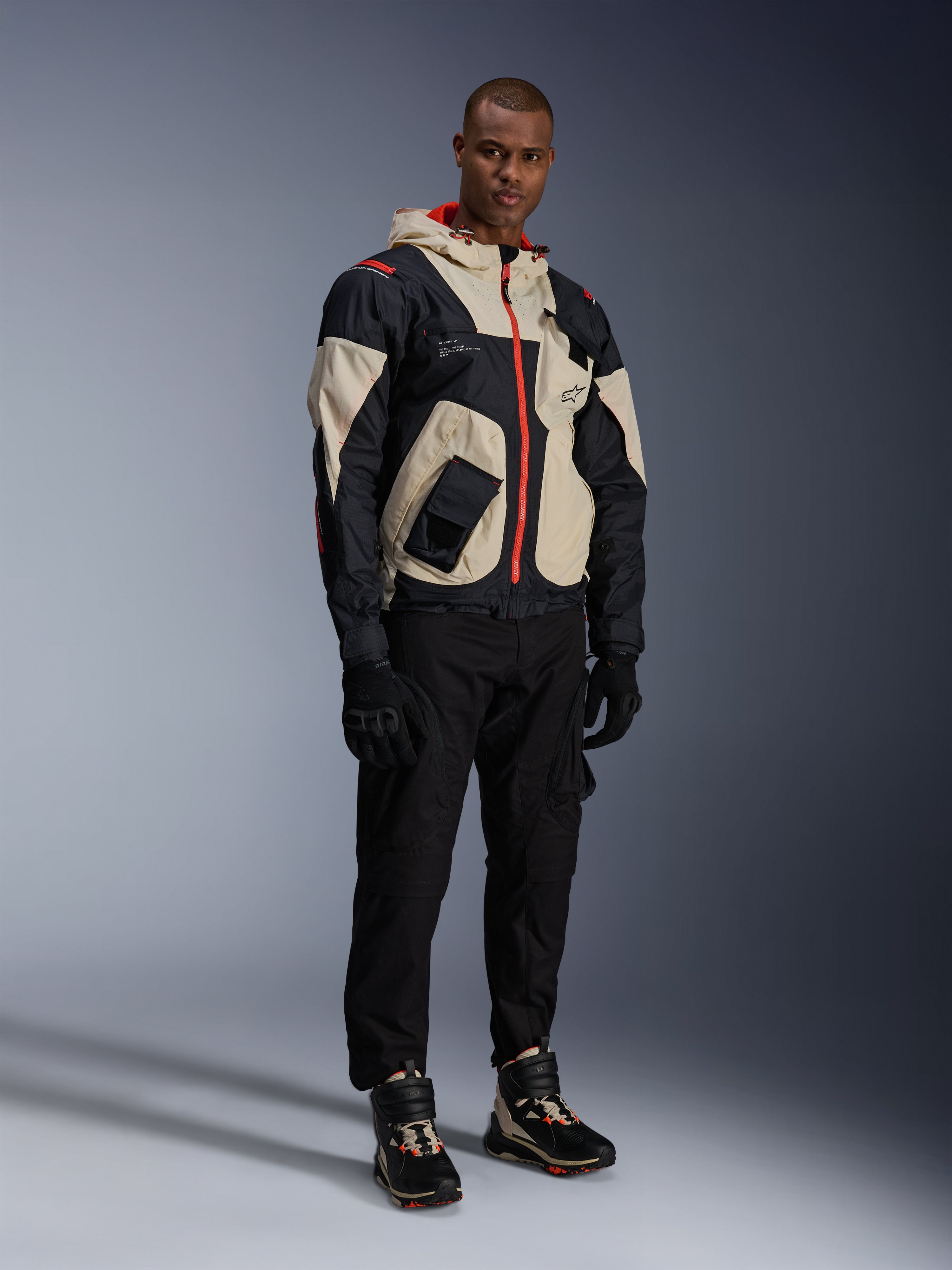 Hombre con equipamiento completo de moto urbana, con zapatillas Alpinestars Speedstreet en Black Almond Hot Orange y chaqueta Mogress Air en negro y crema, pantalones y guantes negros a juego, conjunto protector inspirado en el streetwear para la conducción urbana