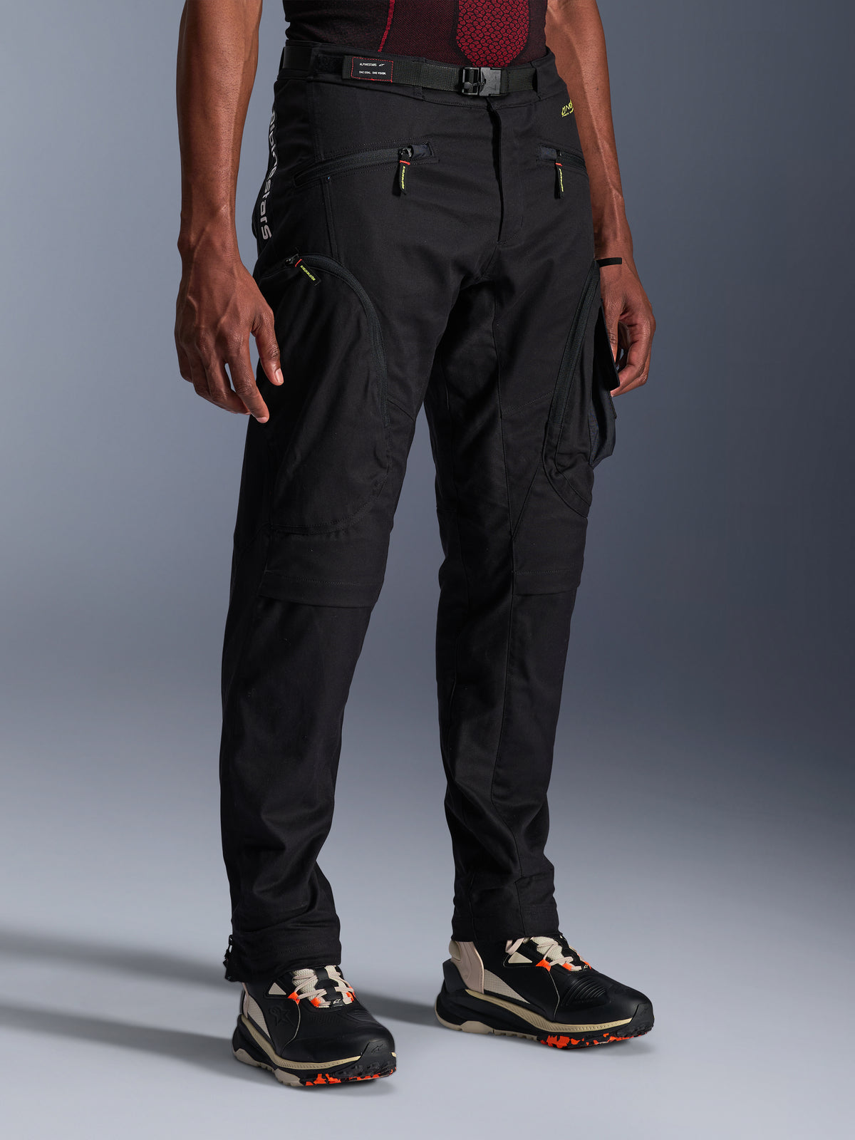 Pantalones Alpinestars Acteon, pantalones de moto negros usados por un modelo, con una silueta moderna y ajustada, bolsillos cargo con cremallera, cinturón ajustable y zapatillas técnicas, equipamiento para conducción urbana