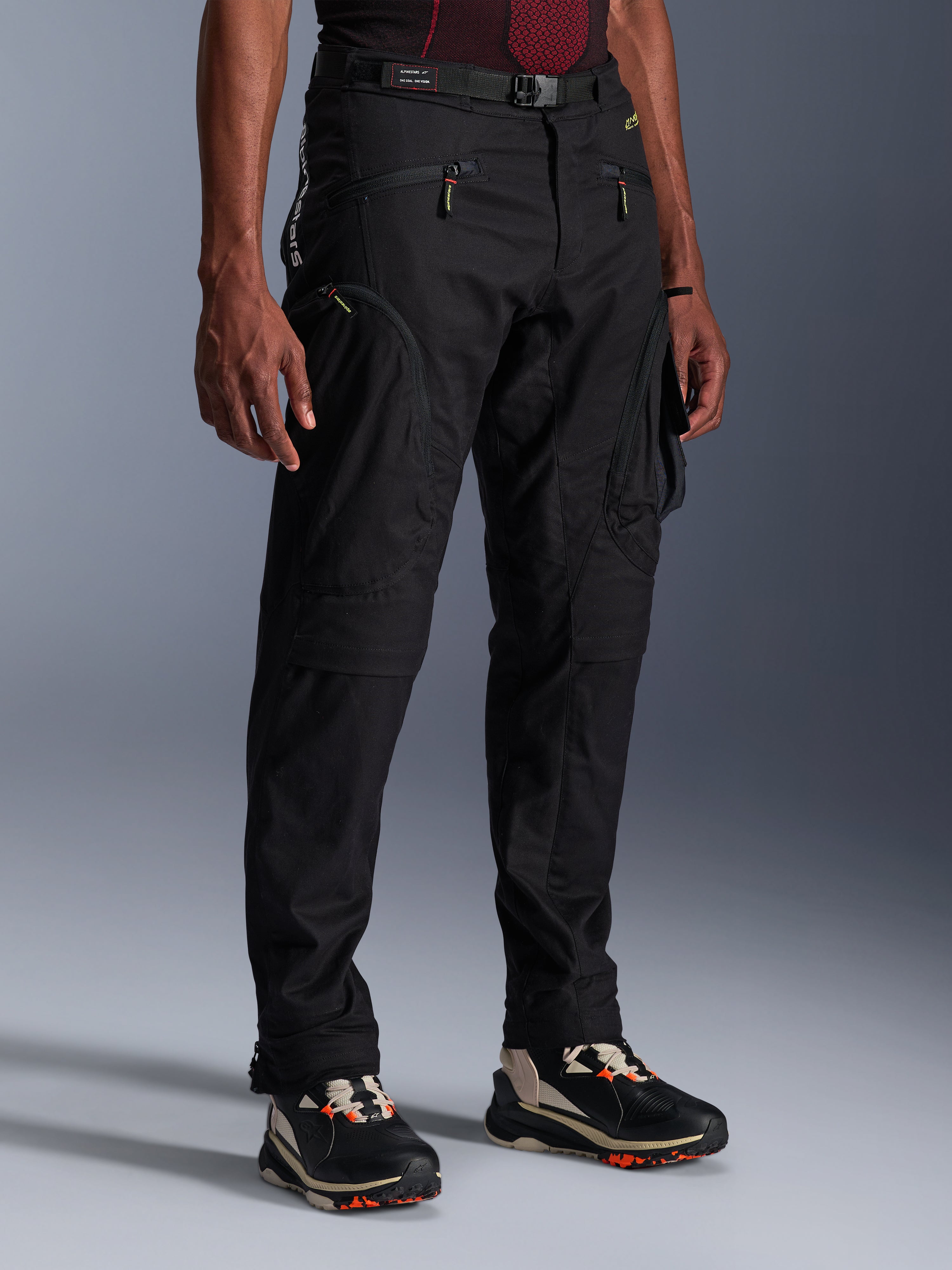 Pantalones Alpinestars Acteon, pantalones de moto negros usados por un modelo, con una silueta moderna y ajustada, bolsillos cargo con cremallera, cinturón ajustable y zapatillas técnicas, equipamiento para conducción urbana