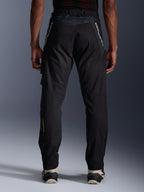Pantalones Alpinestars Acteon, pantalones urbanos de motociclismo, negros, vista trasera que muestra el ajuste entallado, logotipos blancos en la parte superior de las piernas y logotipo amarillo en la parte inferior de la pantorrilla, aberturas ajustables en las piernas con cremalleras, combinados con zapatillas color crema