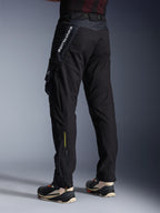 Pantalones Alpinestars Acteon, pantalones de moto negros, vista lateral y trasera que muestra un ajuste cónico moderno, bolsillo tipo cargo lateral con logotipo, marca Alpinestars blanca vertical en la parte superior del muslo, texto amarillo 'Alpinestars Protects' en la parte inferior de la pierna, equipamiento de conducción urbano contemporáneo