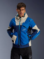Male model wearing the Alpinestars Mogress Air Jacket in Blue Almond, urban motorcycle jacket with bright blue and navy color-blocking, cream accents on the hood and pockets, technical ripstop fabric with utility pockets, modern motorsport-inspired streetwear
