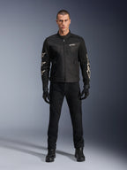 Modelo masculino con la chaqueta Alpinestars T-Dyno Air, negra, chaqueta textil de moto ligera con malla 3D transpirable, logos de estrellas blancas en las mangas, combinada con pantalones, guantes y botas negros, vista frontal de pie